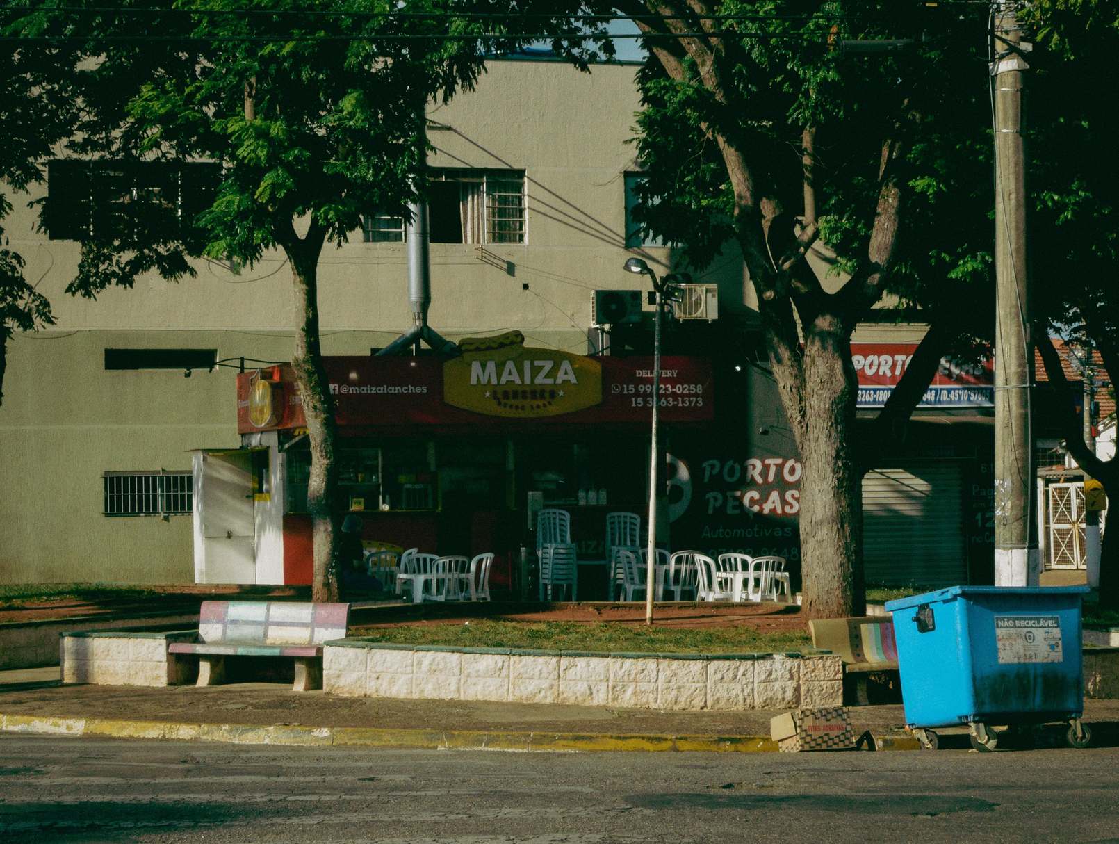 Urban shopping street with pedestrians and storefronts, street scene featuring local market shops under trees